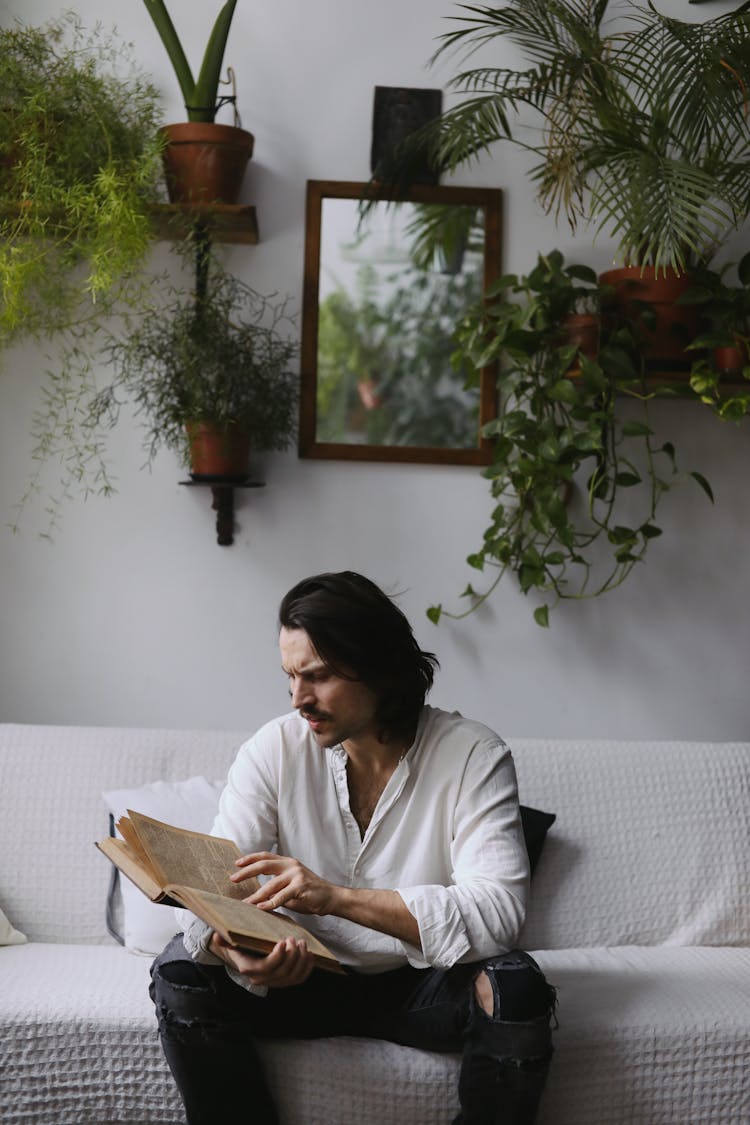 A Man Reading A Book On A Couch