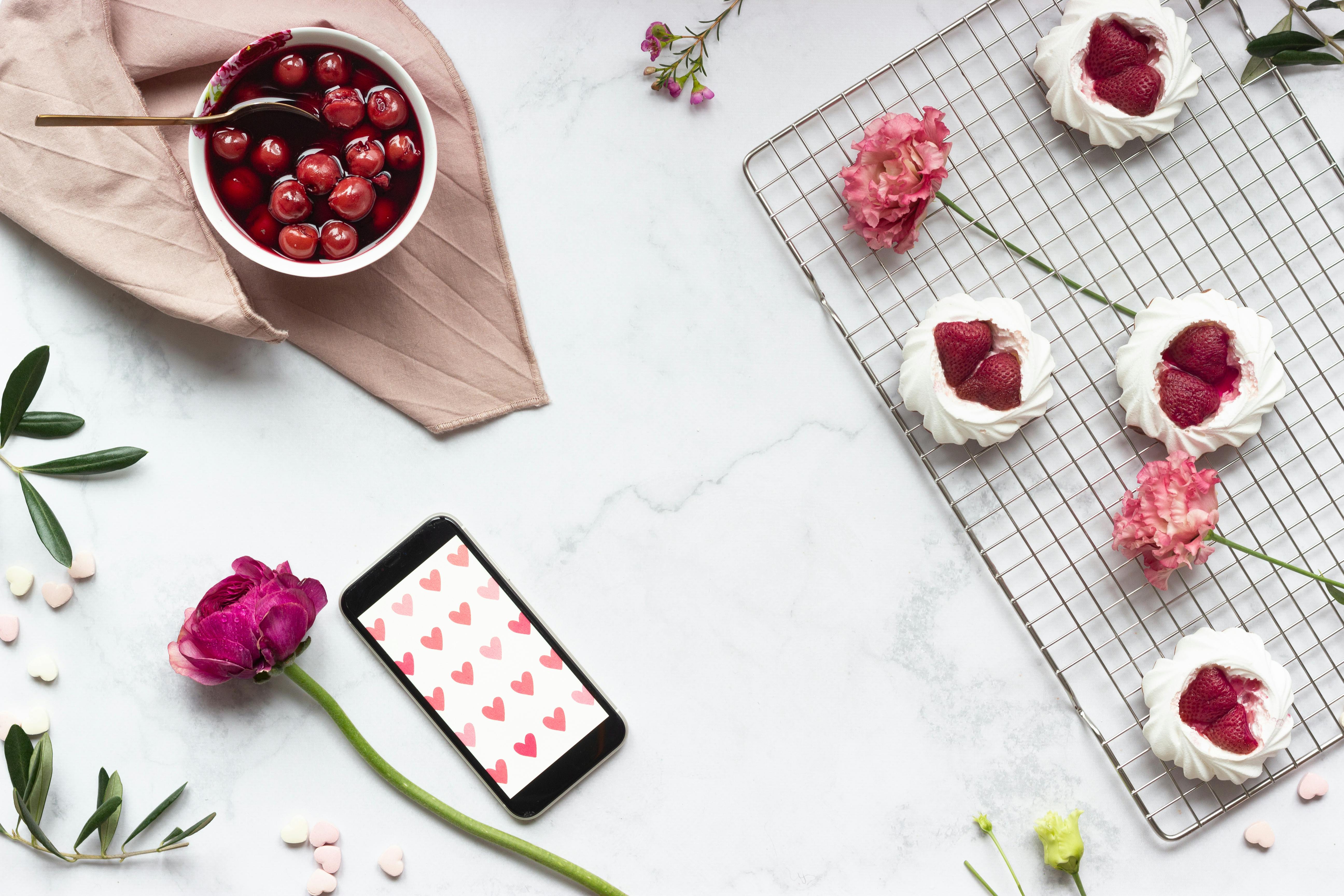 Artistic flat lay of pavlova desserts with strawberries and cherries on a marble surface, enhanced with floral decor.