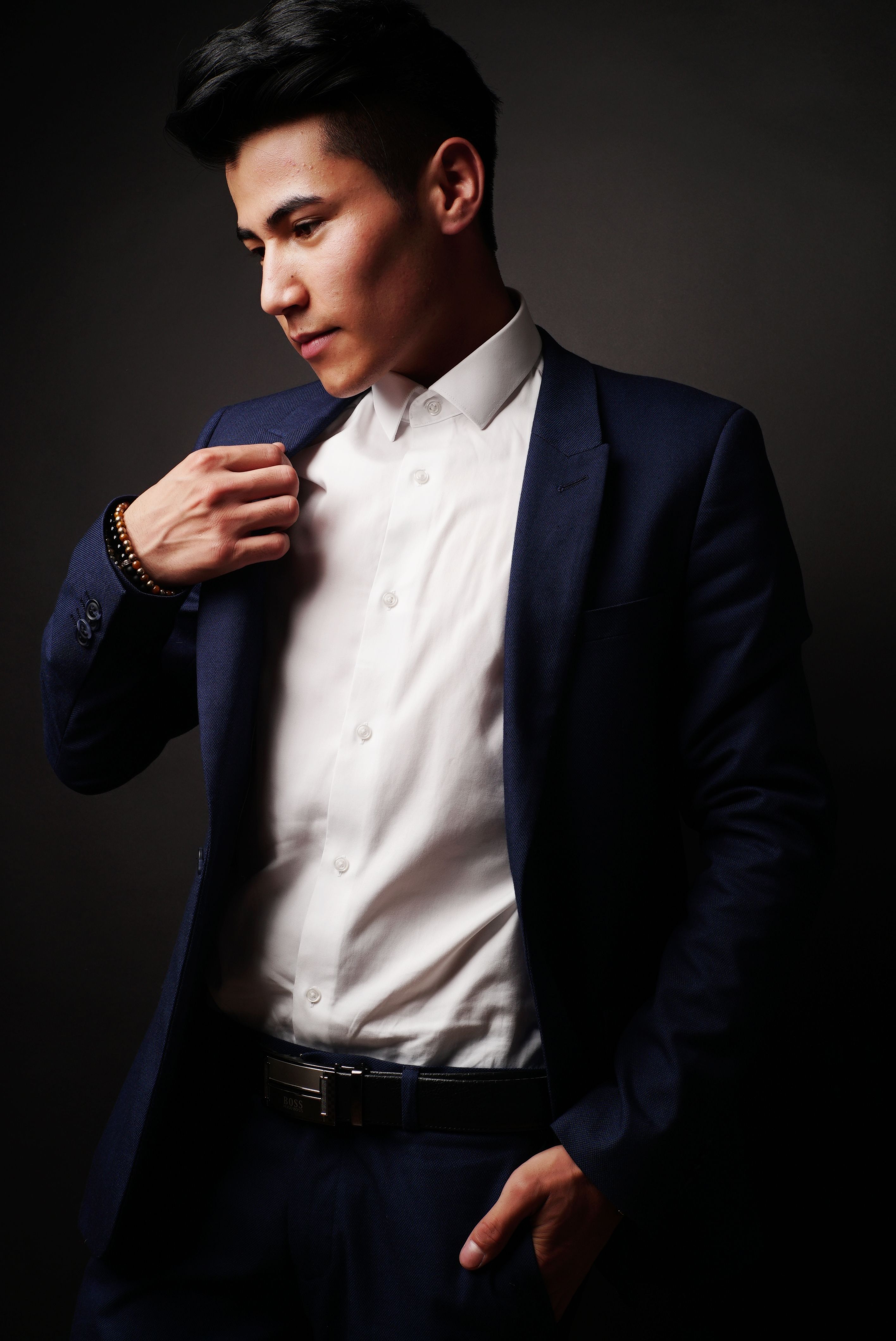 A young man in a blue suit poses confidently indoors during a photoshoot.