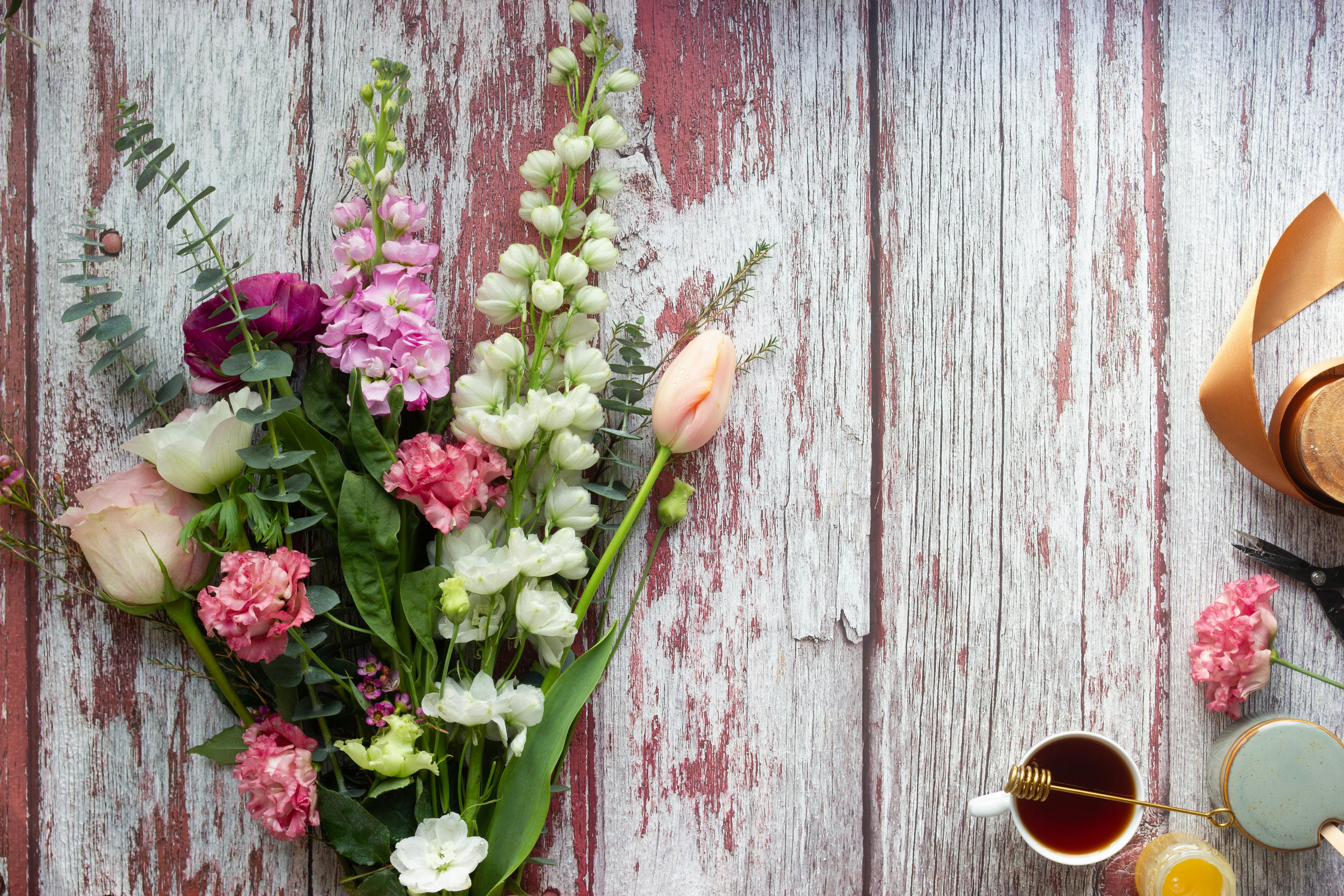 A colorful bouquet of flowers on a rustic wood background with tea and ribbon.