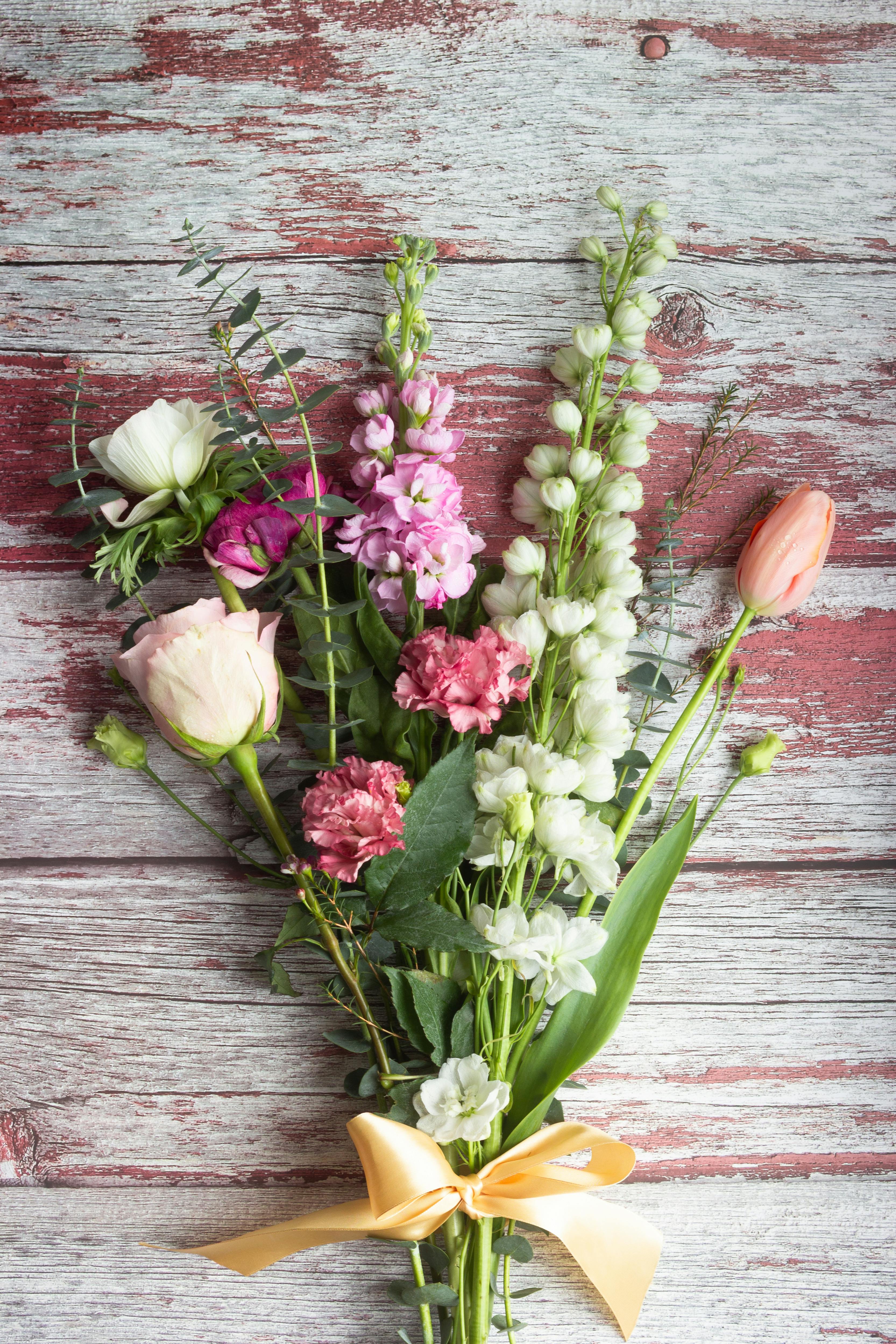 Charming spring bouquet with assorted flowers on a rustic wooden surface, tied with a yellow ribbon.