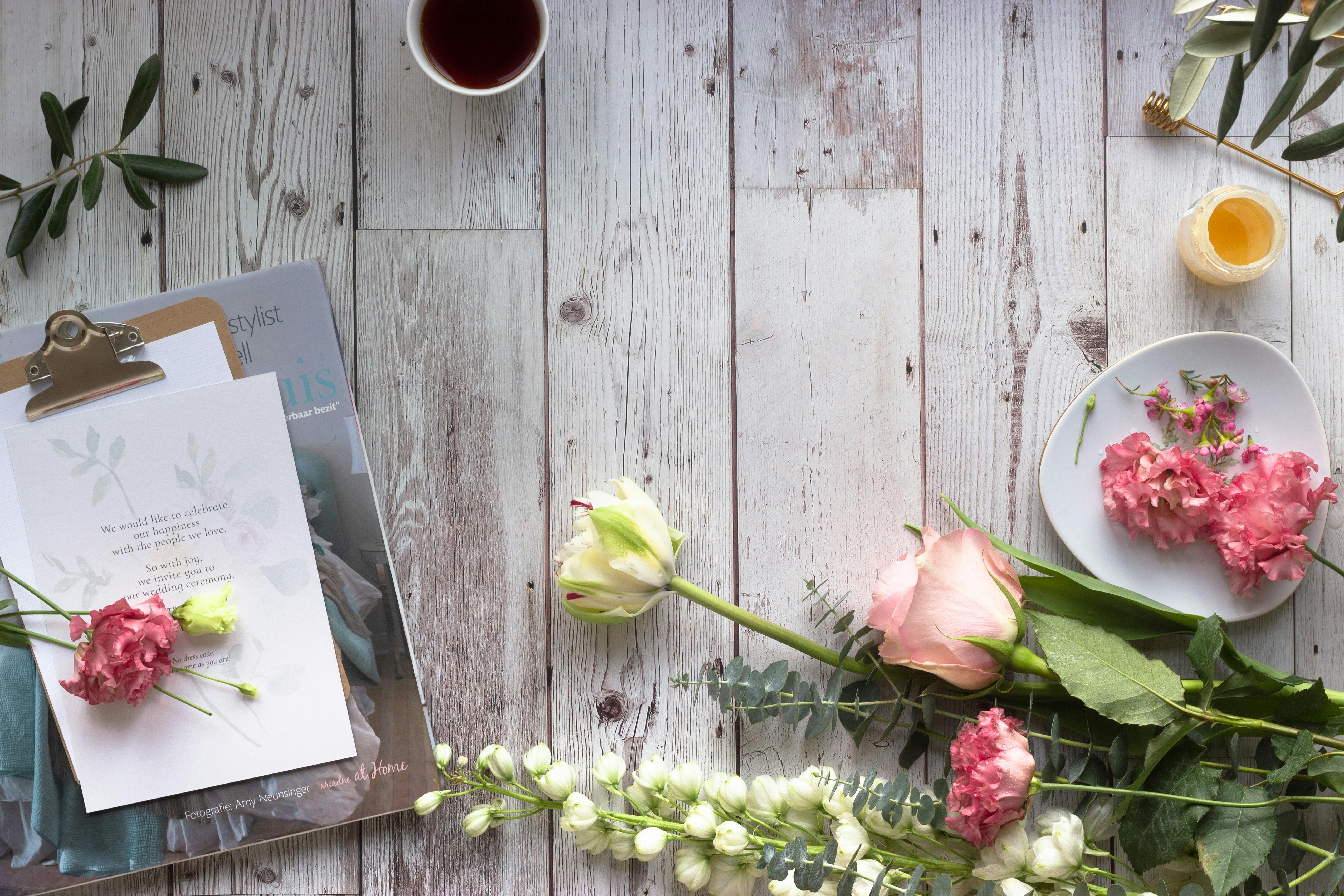 Beautiful flat lay of flowers, clipboard, and a cup of tea on a rustic wooden surface.