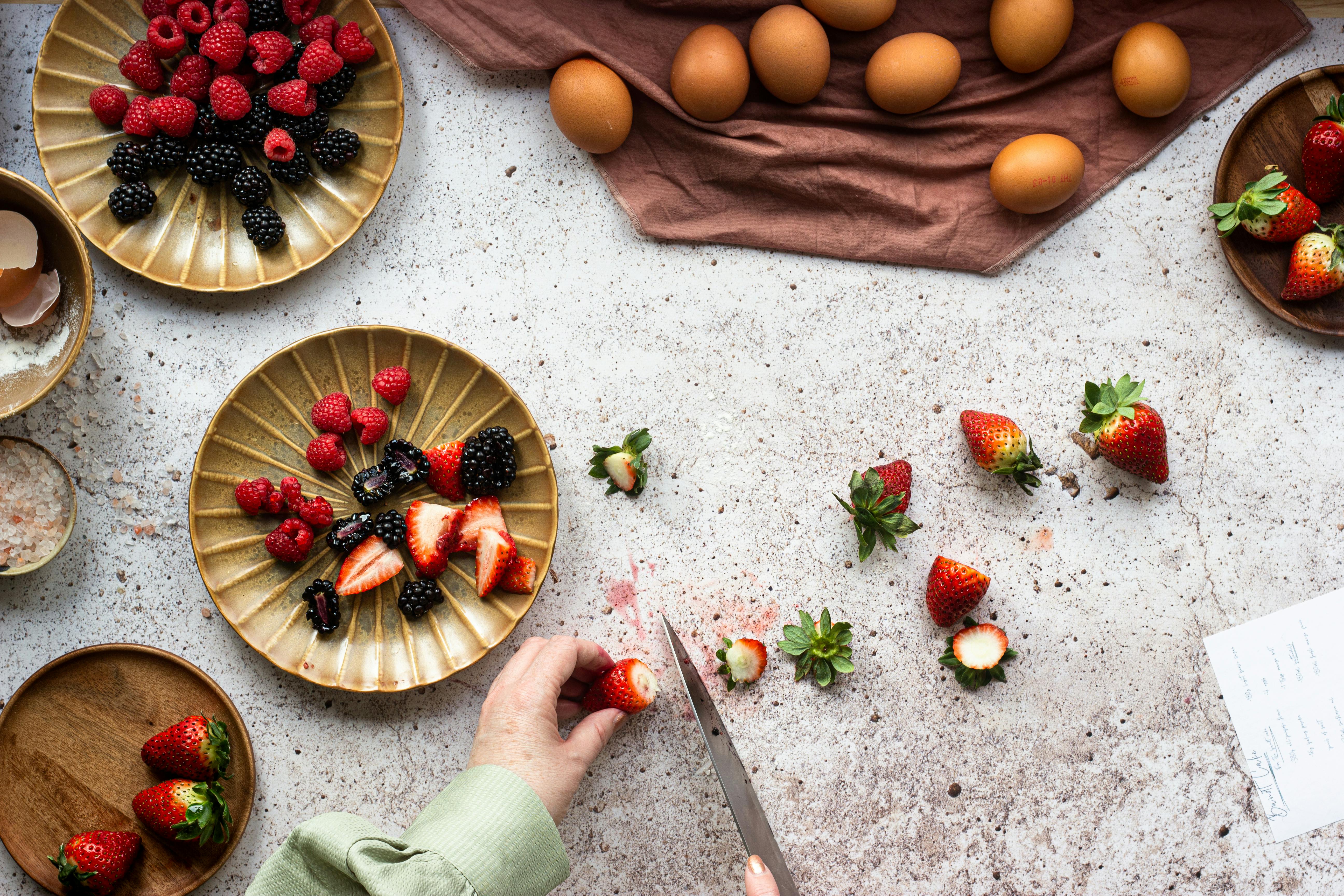 Top view of fresh berries and eggs preparation, featuring hand-cut strawberries in a rustic kitchen setting.
