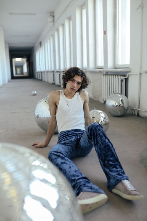 Free Young adult in a stylish outfit sitting in a modern hallway surrounded by reflective spheres. Stock Photo