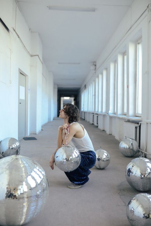 Free Caucasian adult squats in hallway surrounded by shiny disco balls. Stock Photo