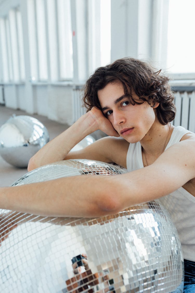 A Man In A White Tank Top Hugging A Disco Ball