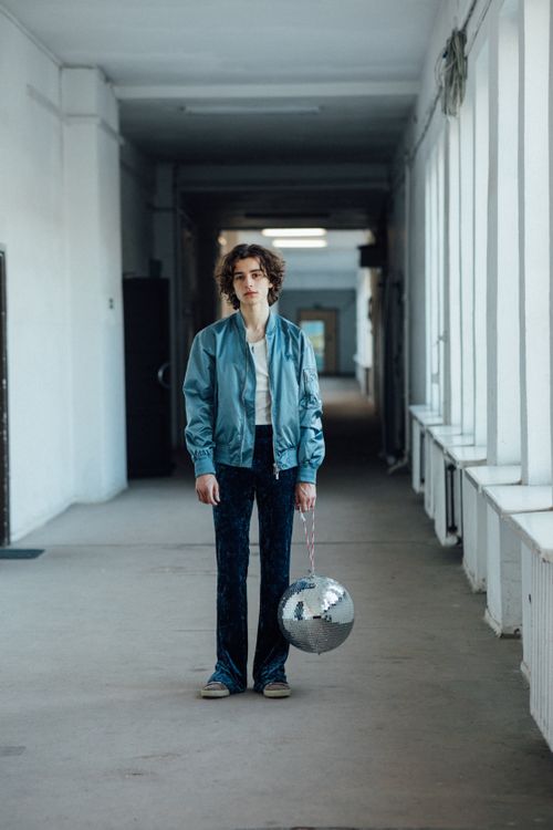 Free Young adult with a blue jacket holding a disco ball in a minimalist hallway. Stock Photo
