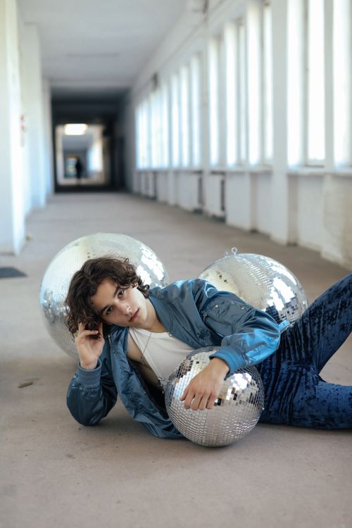 Free A stylish young adult poses with disco balls in a bright hallway. Stock Photo