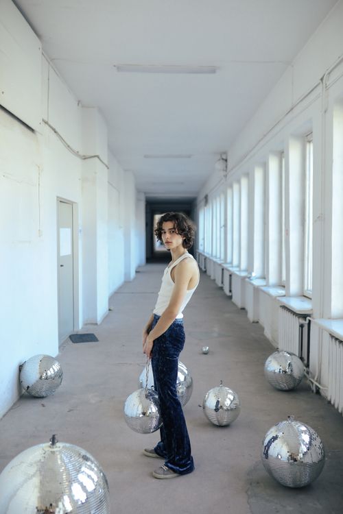 Free Caucasian man in blue jeans and tank top standing in sunny hallway with disco balls. Stock Photo