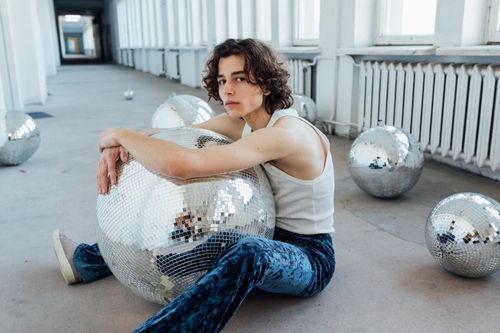 Free A young man in a hallway posing with disco balls, wearing blue jeans and a white tank top. Stock Photo
