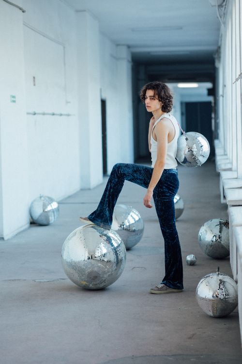 Free Stylish young adult in velvet pants and tank top posing with reflective disco balls. Stock Photo
