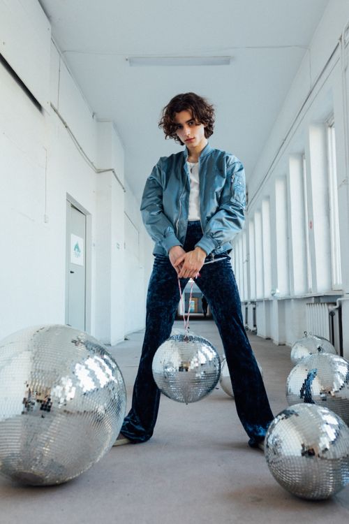 Free Trendy young adult with curly hair holding a disco ball in a modern hallway setting. Stock Photo