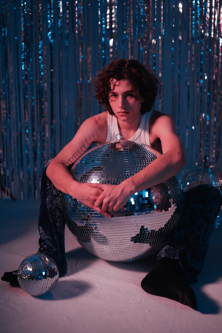 A Man In A White Tank Top Hugging A Disco Ball