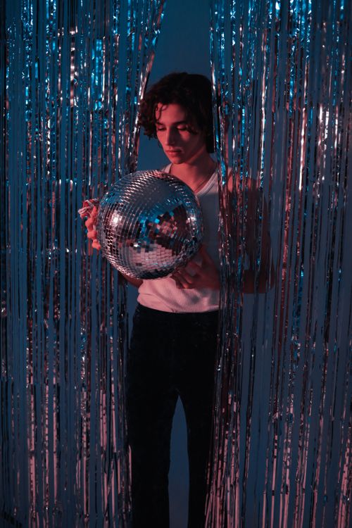 Free A man in a retro setting with a disco ball and foil curtain, capturing vintage vibes. Stock Photo