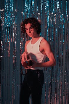 Young man posing indoors with foil curtain backdrop and retro telephone, exuding a stylish retro vibe.