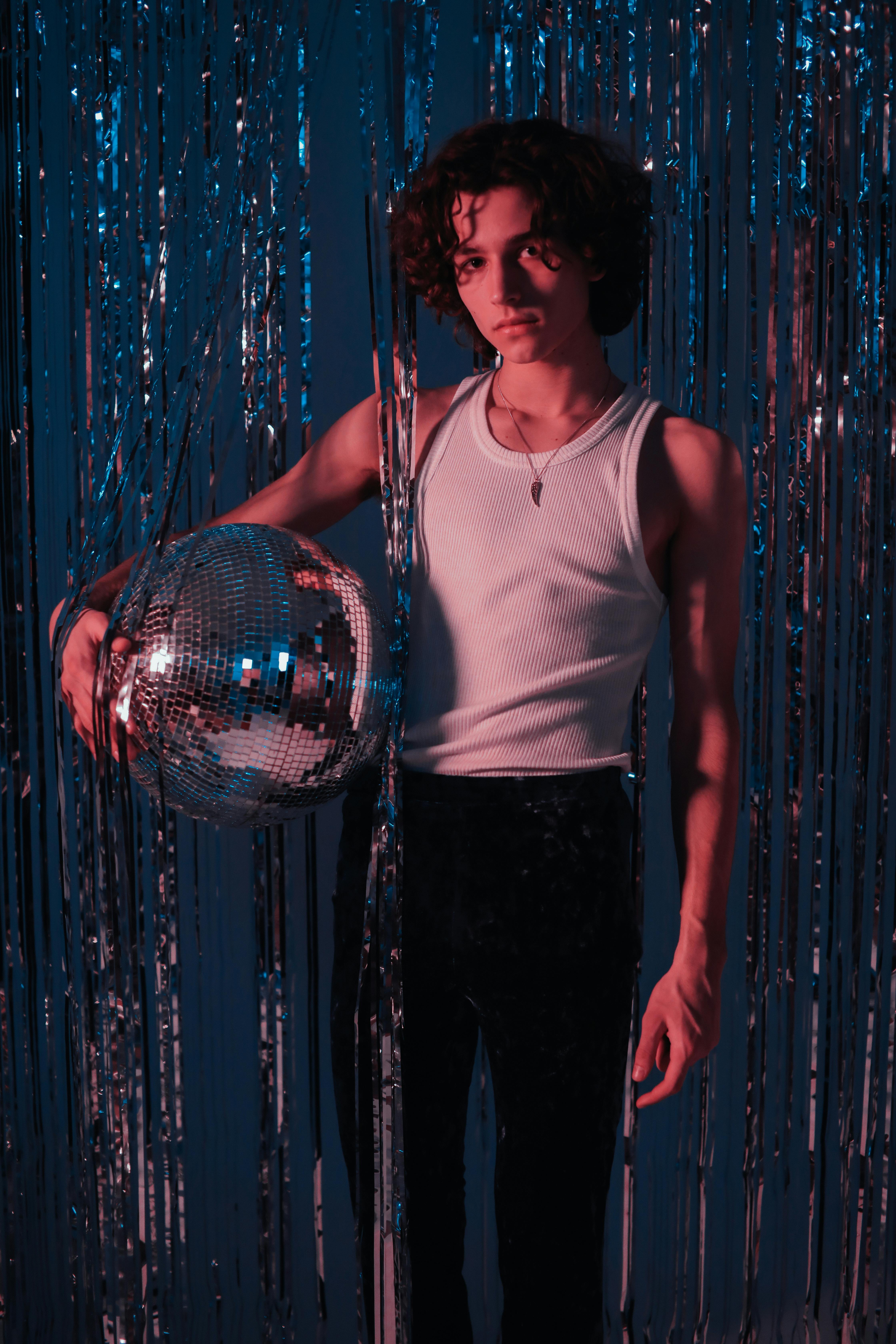 man in white tank top and black pants standing beside blue curtain