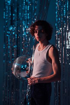 Young man with curly hair holding a disco ball in a retro setting