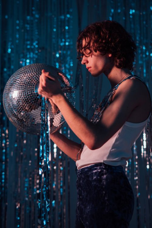 Free A stylish teenager with curly hair holding a disco ball in a retro-themed setting. Stock Photo