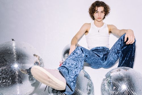 Free Fashionable young man in a white tank top and blue pants surrounded by disco balls in a modern setting. Stock Photo