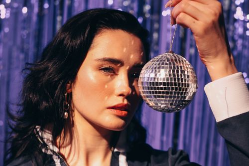 Free A stylish brunette woman poses with a reflective disco ball, capturing a retro, glamorous vibe. Stock Photo
