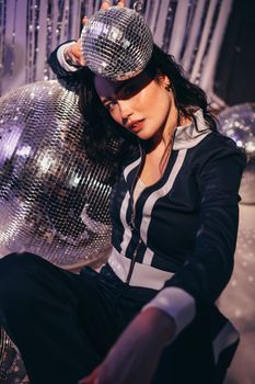 Stylish woman posing with disco balls in a retro fashion setting.