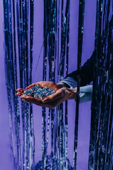 Close-up of hands holding mini disco balls through shimmering curtains, ideal for party themes.