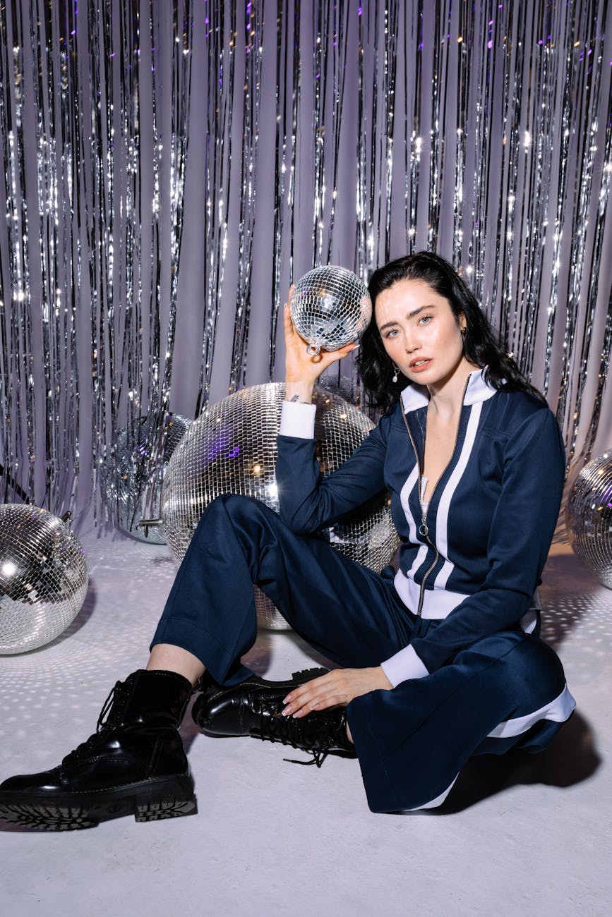 Stylish woman posing in retro disco setting with shimmering background.