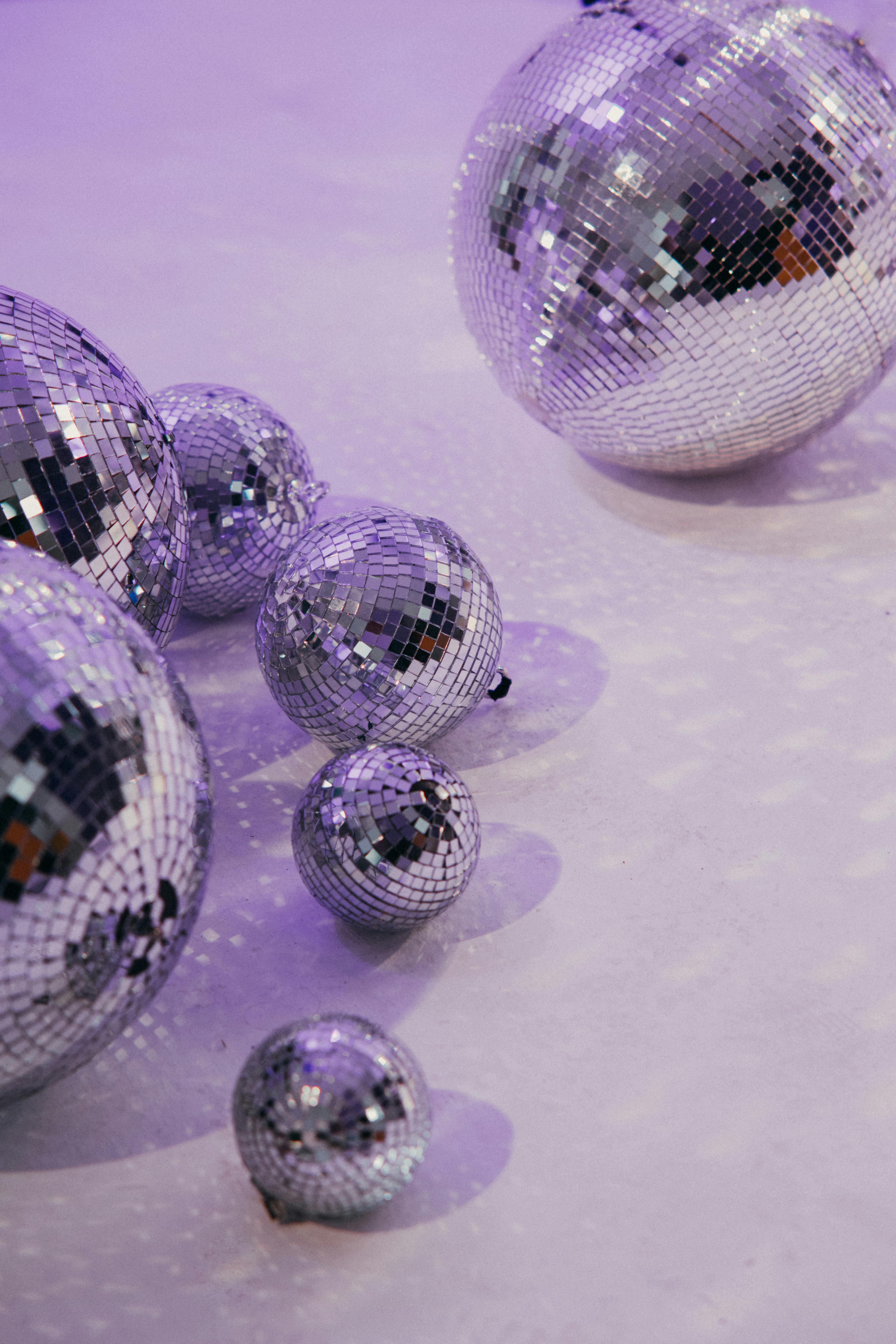 A collection of disco balls casting reflections on a purple lit floor, creating a vibrant atmosphere.