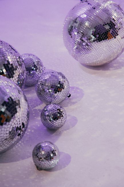 A collection of disco balls casting reflections on a purple lit floor, creating a vibrant atmosphere.
