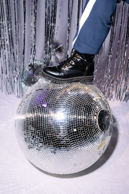 A black boot stylishly perched on a glittering disco ball in a festive scene.