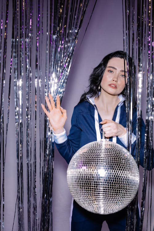 Photo of a Woman in a Blue Tracksuit Holding a Disco Ball