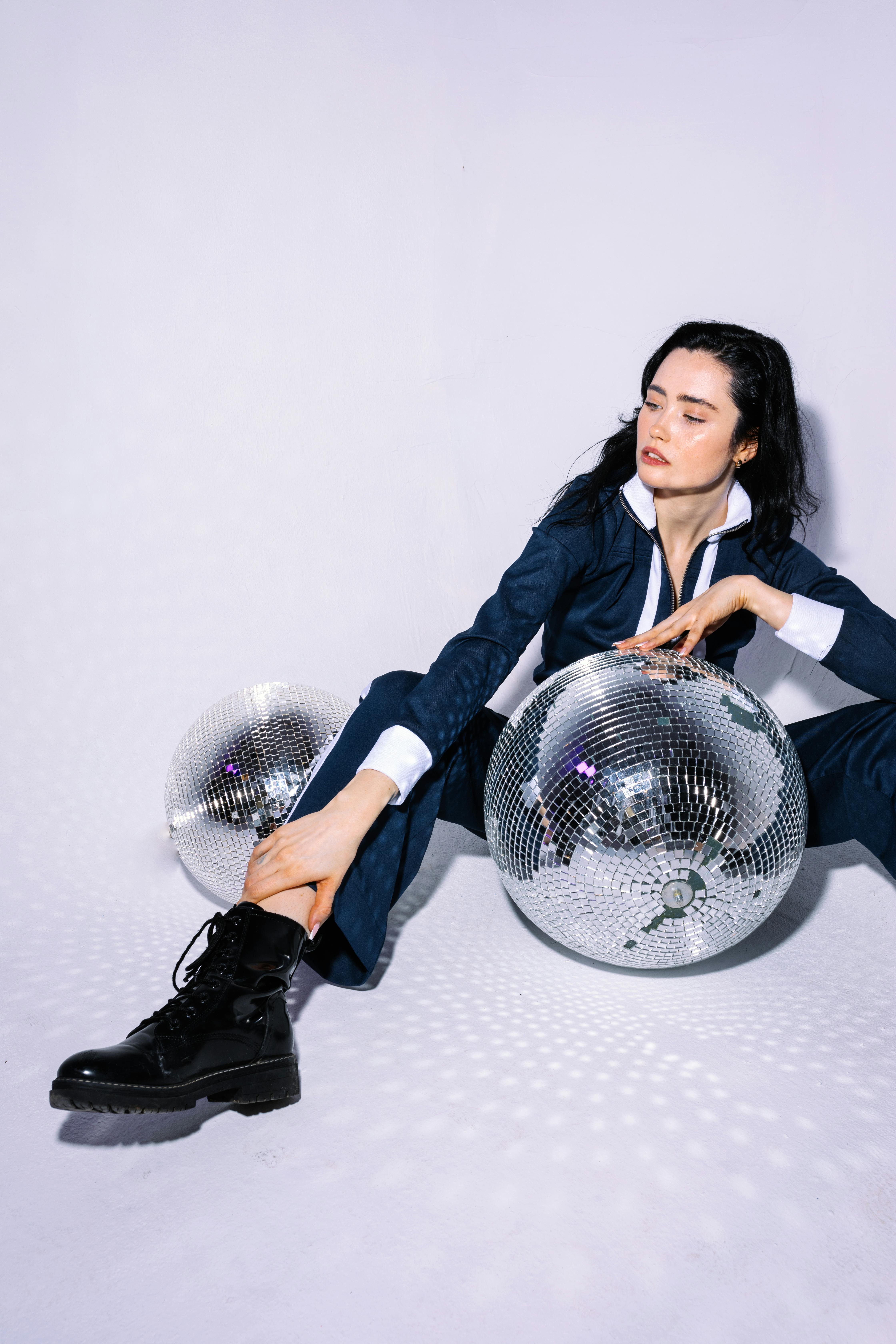 photo of a woman in a white and blue tracksuit sitting near disco balls