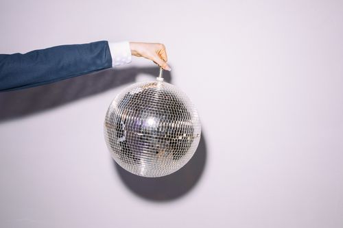 Free A hand in a suit holds a reflective disco ball against a neutral wall. Bright lighting. Stock Photo