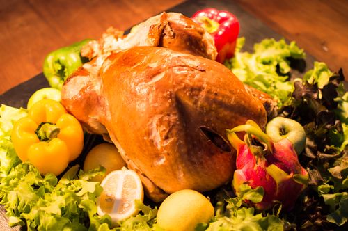 Free Close-up of a roasted chicken surrounded by fresh bell peppers and lettuce, perfect for dinner. Stock Photo