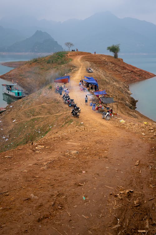 Motorcycles parked along path with canopy tents on hill washed by lake in hazy valley