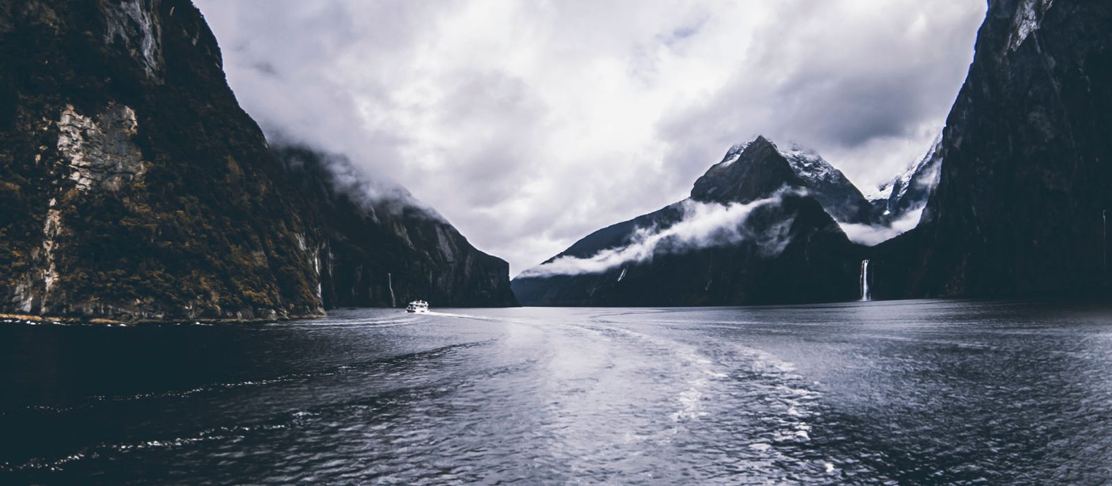 Breathtaking view of Milford Sound fjord with dramatic clouds and serene waters.