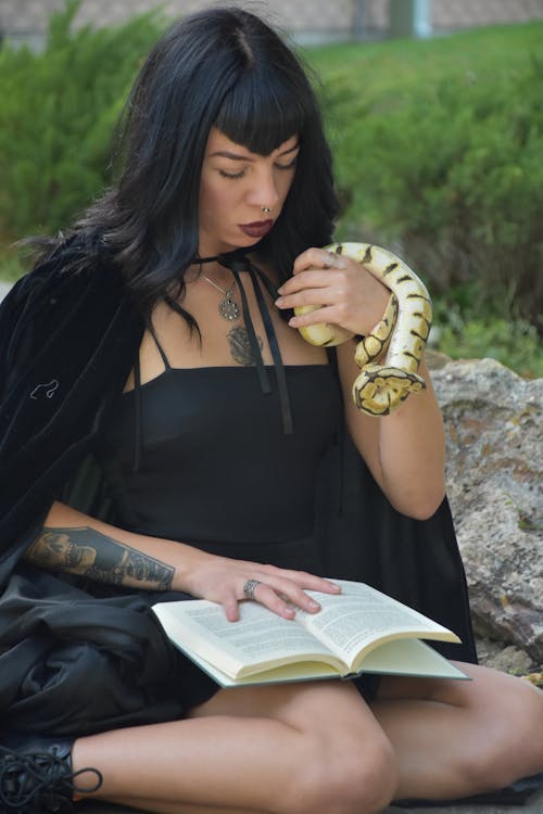 Photo of a Woman Reading a Book while Holding a Snake