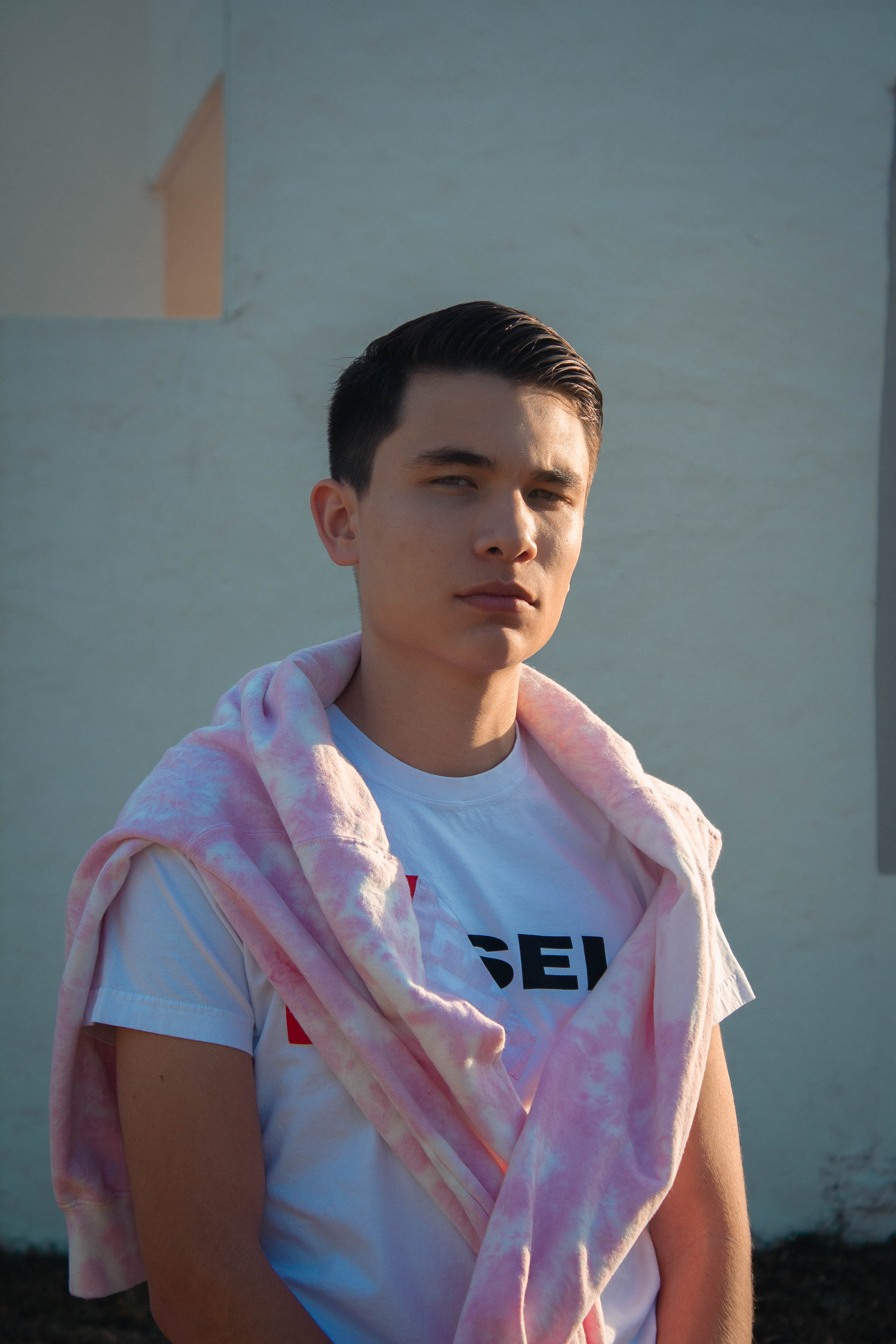 Portrait of a young man posing outdoors with a serious expression wearing casual clothing.