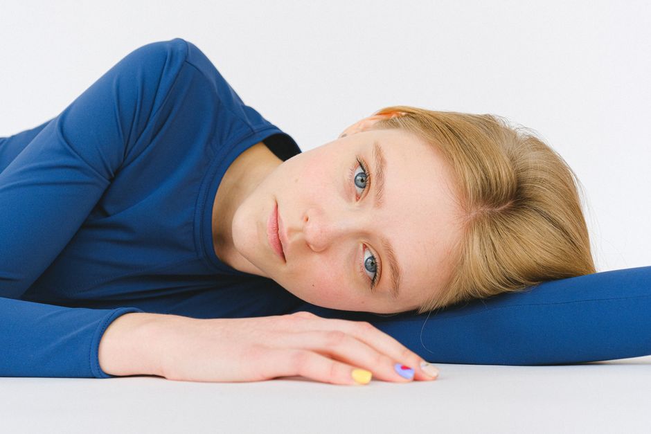 Unemotional young female in blue clothes lying on white floor and looking at camera in studio