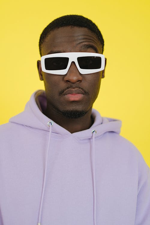 Arrogant African American male in purple hoodie and trendy sunglasses looking at camera against yellow background