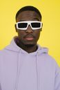 Arrogant African American male in purple hoodie and trendy sunglasses looking at camera against yellow background