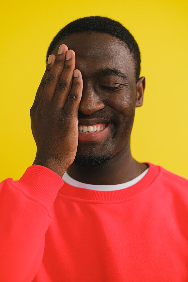 Cheerful Black Man Covering Eye With Hand In Studio