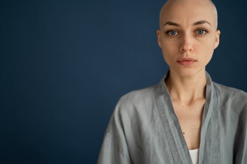 Crop young bald female in gray robe looking at camera against dark wall in studio