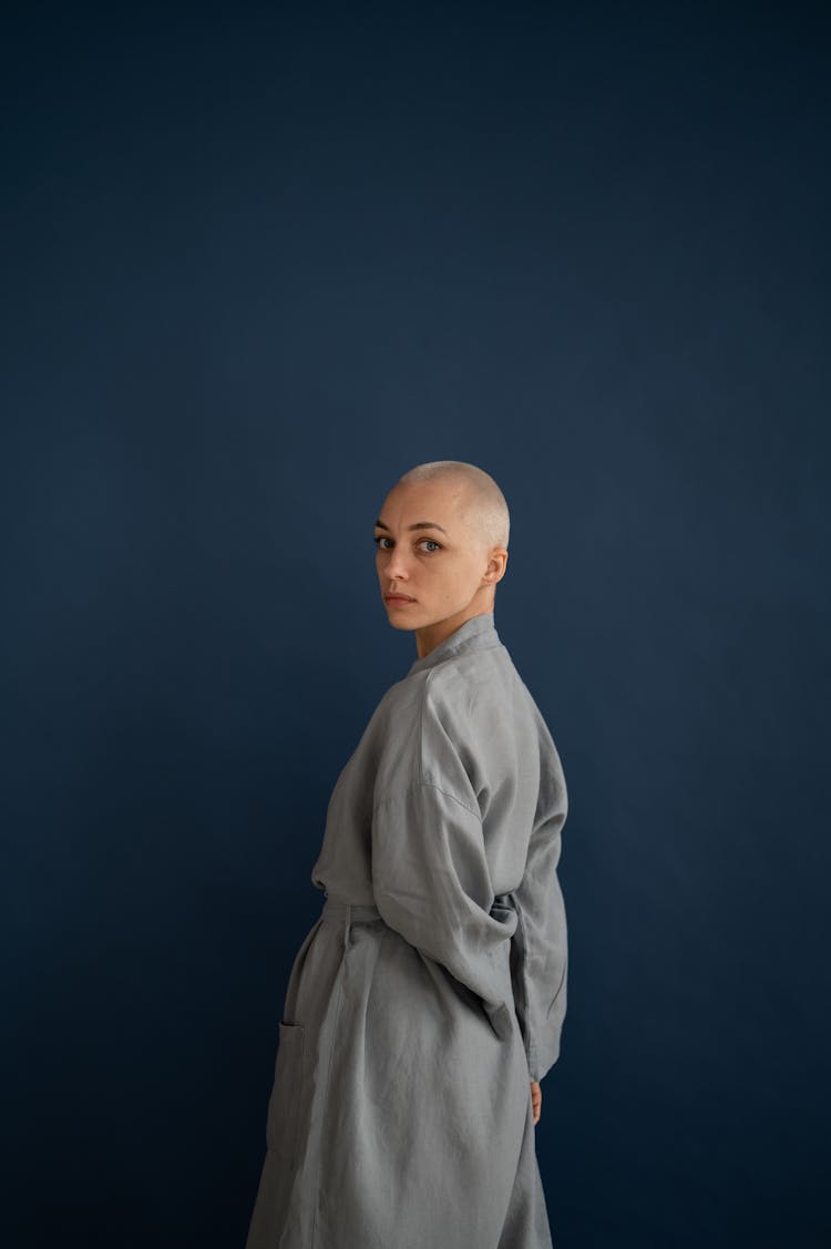 Calm Bald Woman In Robe Standing In Dark Studio