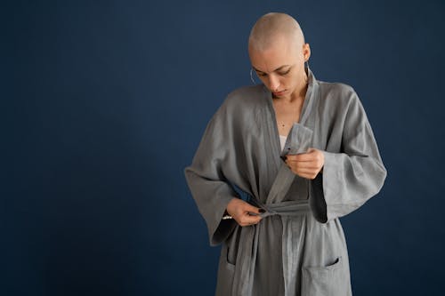 Unemotional bald woman tying robe in studio