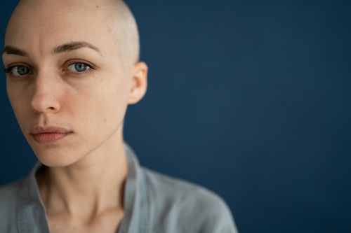 Free Crop wistful bald female in gray wear looking at camera thoughtfully against dark blue wall Stock Photo