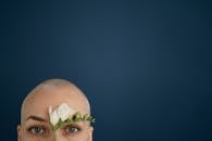 Crop bald woman touching face with tender flower