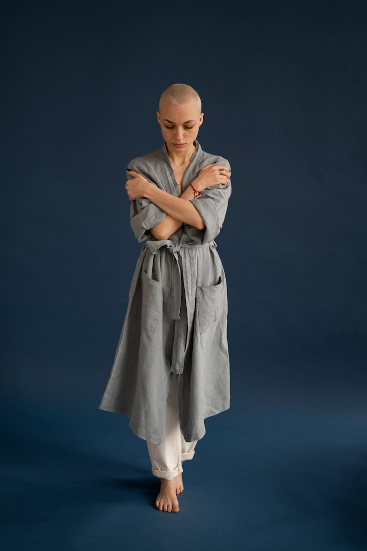 Wistful Bald Woman In Robe Embracing Self In Studio