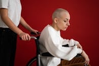 Crop assistant pushing wheelchair with sick patient on red background