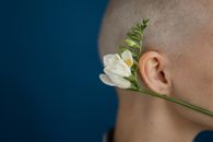 Side view of crop unrecognizable person with shaved head and blossoming flower representing cicatrice after brain tumor operation